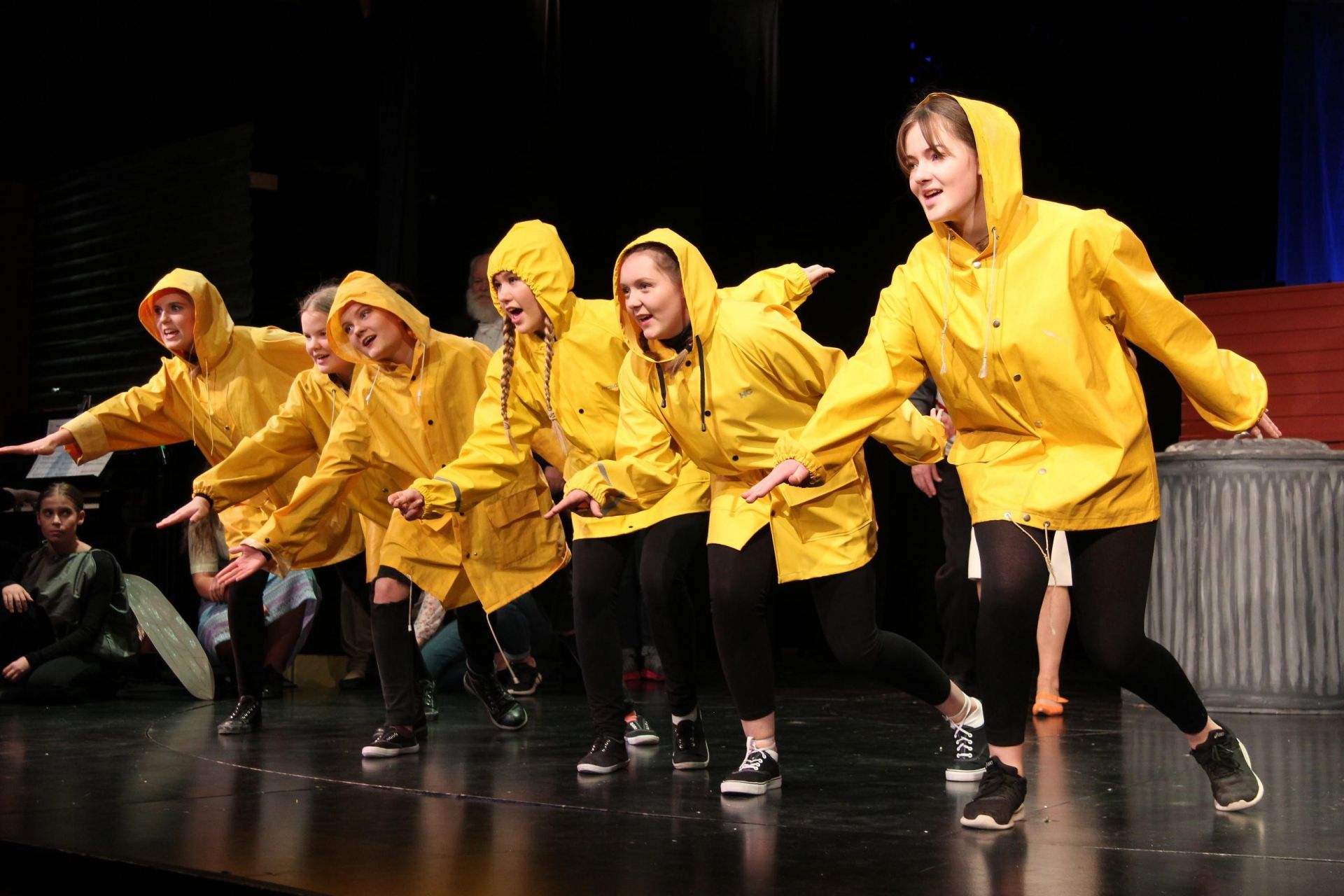 Ungdomar på rad på scenen. Alla klädda i gula regnrockar.